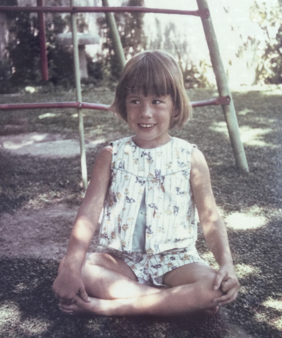 Lucy Ramsdell as a young girl, sitting cross-legged in a sunny backyard